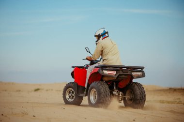 Kasklı bir adam çölde ATV 'ye biniyor, aksiyon manzaralı.