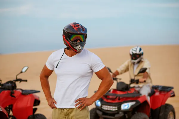 Dva závodníci v helmách pózují poblíž atv v poušti — Stock fotografie