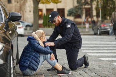 Erkek polis memuru şokta olan bir kadın sürücüyü sakinleştiriyor.