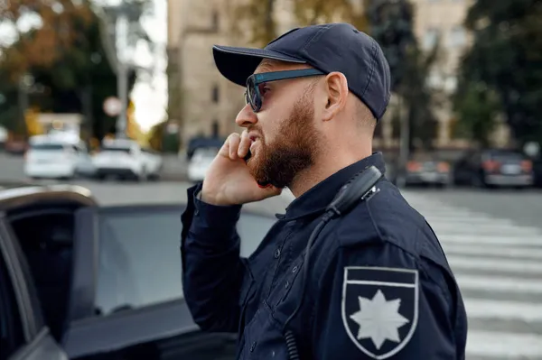 Policjant rozmawiający przez telefon, parking. — Zdjęcie stockowe