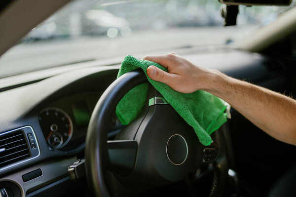 Man wipes car interior with a rag, hand auto wash station. Car-wash industry or business. Male person cleans his vehicle from dirt outdoors
