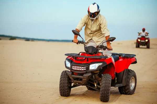 El hombre posa en el atv, cuesta abajo cabalgando en las arenas del desierto —  Fotos de Stock