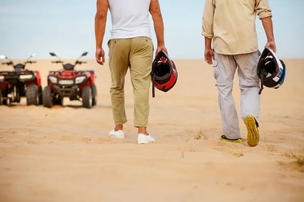 Dva závodníci drží helmy v blízkosti atv v poušti — Stock fotografie