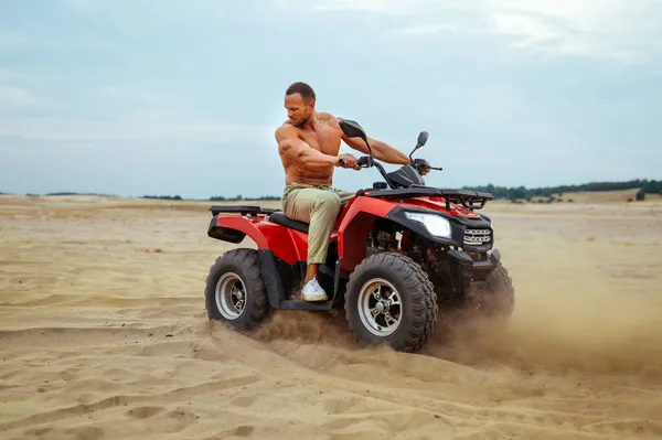 Brutální muž pózuje na atv v pouštních píscích, quadbike — Stock fotografie