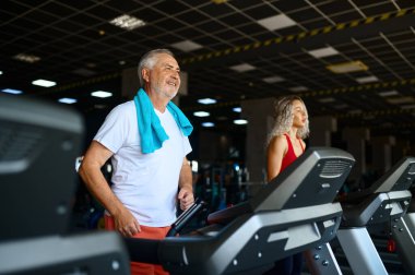 Yaşlı bir adam ve kadın antrenör spor salonunda koşu bandında