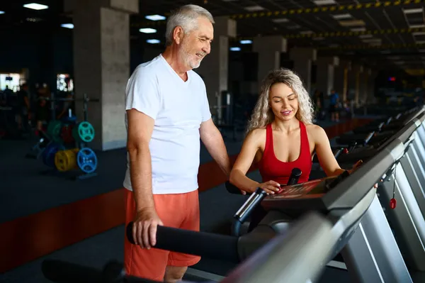 Viejo en la cinta de correr, entrenador personal femenino —  Fotos de Stock