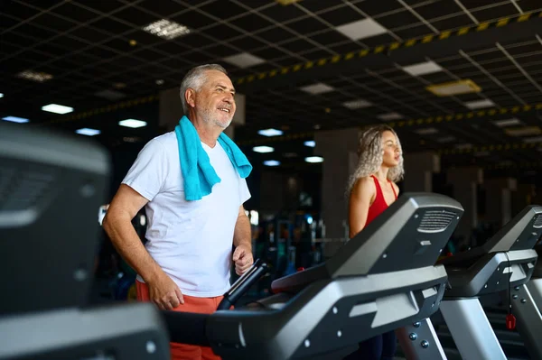 Elderly man and female trainer on treadmill in gym