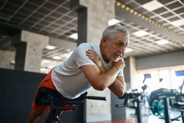 Starszy mężczyzna w odzieży sportowej ćwiczący mięśnie brzucha, siłownia — Zdjęcie stockowe