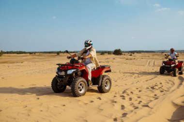 Kasklı ve gözlüklü adamlar çölde ATV 'ye biniyorlar.