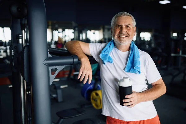 Old man with bottle of water and towel in gym