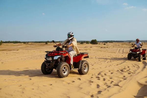 Men in helmets and glasses ride on atv in desert — Stock Photo, Image