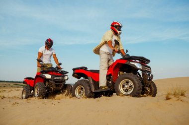 Kasklı bir adam çölde ATV 'ye biniyor.