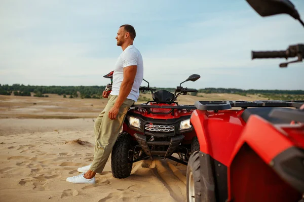 Brutális férfi pózol közelében atv a sivatagban, quadbike — Stock Fotó