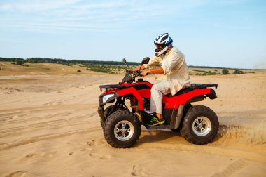 Kasklı bir adam çölde ATV 'ye biniyor.