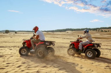 Kask takan iki adam çölde ATV 'ye biniyor.