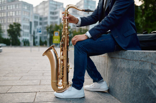 Male saxophonist with sax, buildings on background