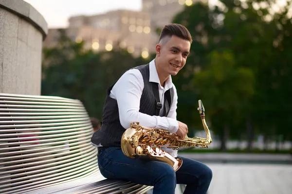 Saxophonist sitting on the bench in city park — Stock Photo, Image