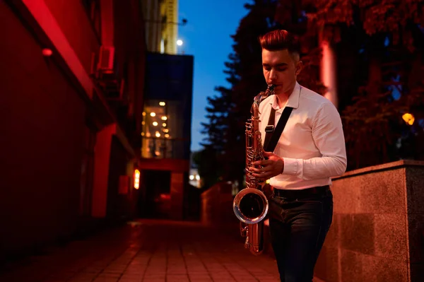 Jovem saxofonista toca saxofone na rua à noite — Fotografia de Stock