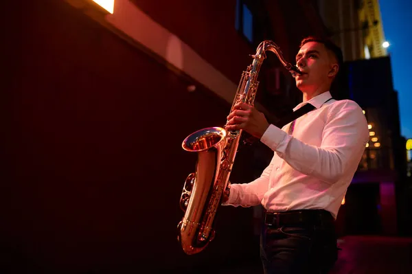 Mladý saxofonista hraje v noci na saxofon na ulici — Stock fotografie