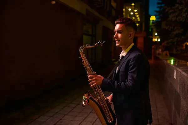 Saxofonista toca el saxo en la calle oscura por la noche — Foto de Stock