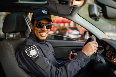 Güneş gözlüklü polis memuru devriye arabasında poz veriyor.