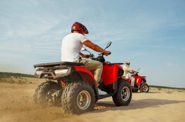Kasklı ve gözlüklü adamlar çölde ATV 'ye biniyorlar.