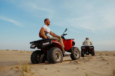 Kasklı bir adam çölde ATV 'ye biniyor.