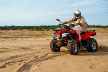Kasklı bir adam çölde ATV 'ye biniyor.
