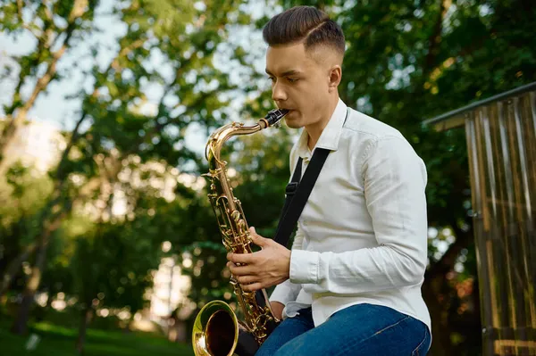 Jovem saxofonista toca saxofone no parque — Fotografia de Stock