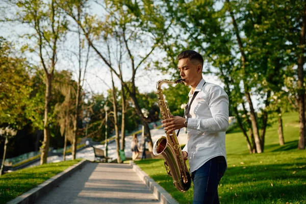 Jovem saxofonista toca saxofone no parque — Fotografia de Stock