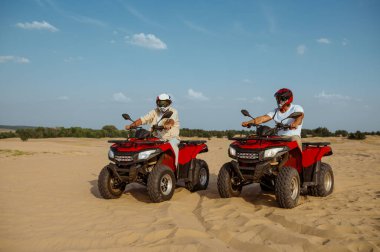 Kasklı ve gözlüklü adamlar çölde ATV 'ye biniyorlar.