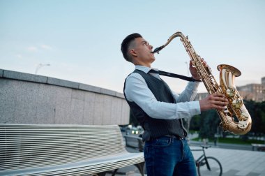Saksafoncu şehir parkındaki bankta melodi çalıyor.