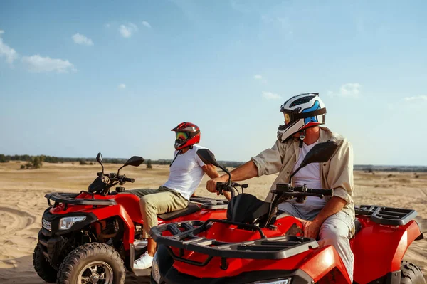 Two men in helmets ride on atv in desert — Stock Photo, Image