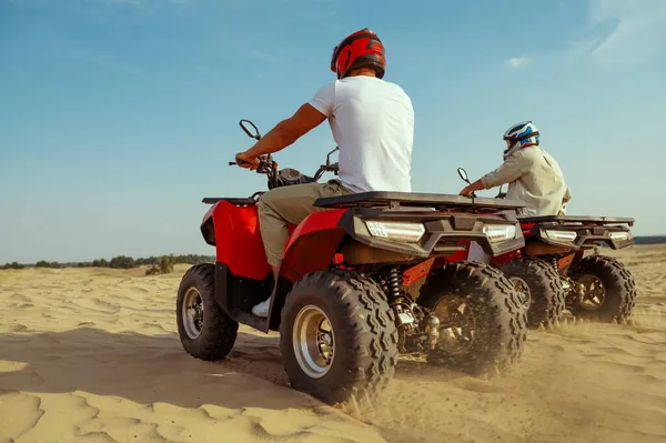 Two men in helmets riding on atv in desert sands — Stock Photo, Image