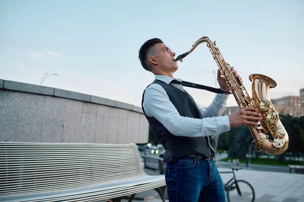 Saksofonista gra melodię na ławce w parku miejskim — Zdjęcie stockowe