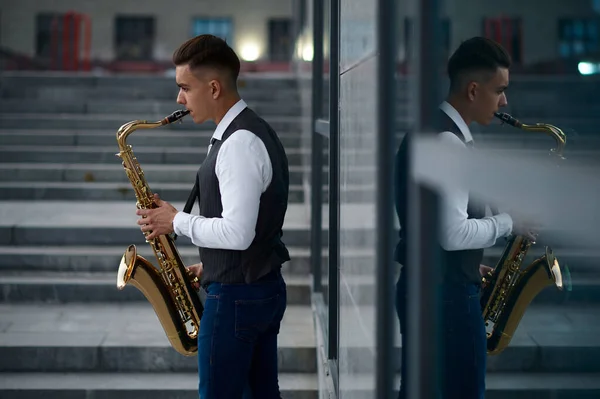 Саксофонист играет мелодию на лестнице на улице — стоковое фото