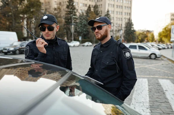 Két férfi rendőr rádión ellenőrzi az autót. — Stock Fotó