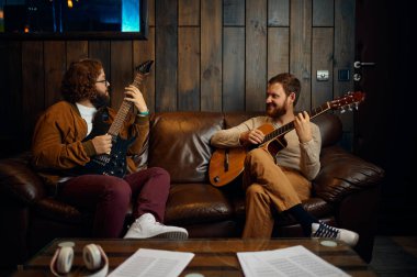 Erkek arkadaşlar evde birlikte gitar çalıyorlar.