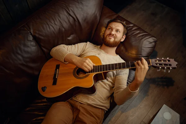Verträumter Mann liegt auf Couch und spielt Gitarre — Stockfoto