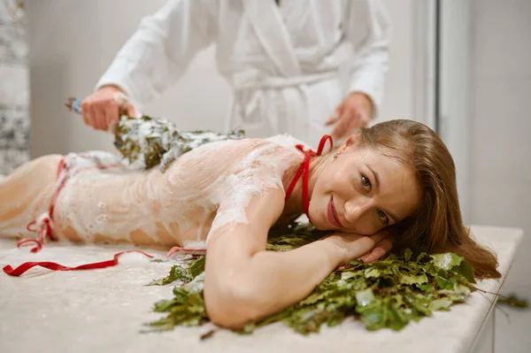 Женщине в ванной делают массаж метлой на пару — стоковое фото