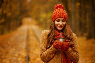 Genç bayan sonbahar parkında çay içiyor.