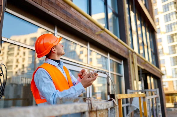 Builder climbing in cradle over building facade — Stockfoto