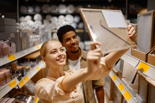 Pareja joven comprando marco de fotos en la tienda — Foto de Stock