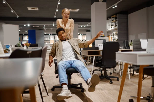 Funny couple riding office chair at shop