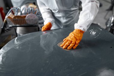 Üniformalı tamirci boyalı araba gövdesi zımparalıyor.