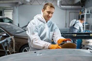 Serviceman polishing car body part in workshop
