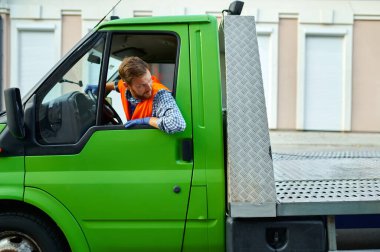 Çekici kamyon şoförü caddeden aşağıya araba taşıyor.