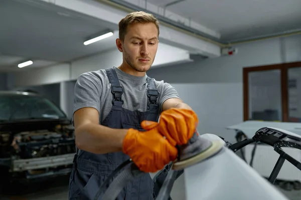 Serviceman polishing car body part in workshop — 스톡 사진