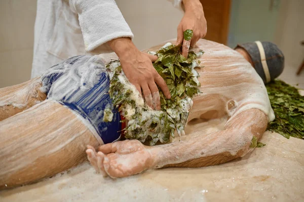 Férfi kap masszázs seprűvel a fürdőben — Stock Fotó