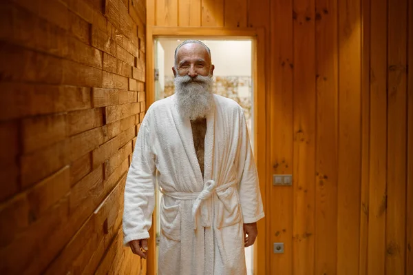 Улыбающийся бородатый мужчина в халате в сауне — стоковое фото